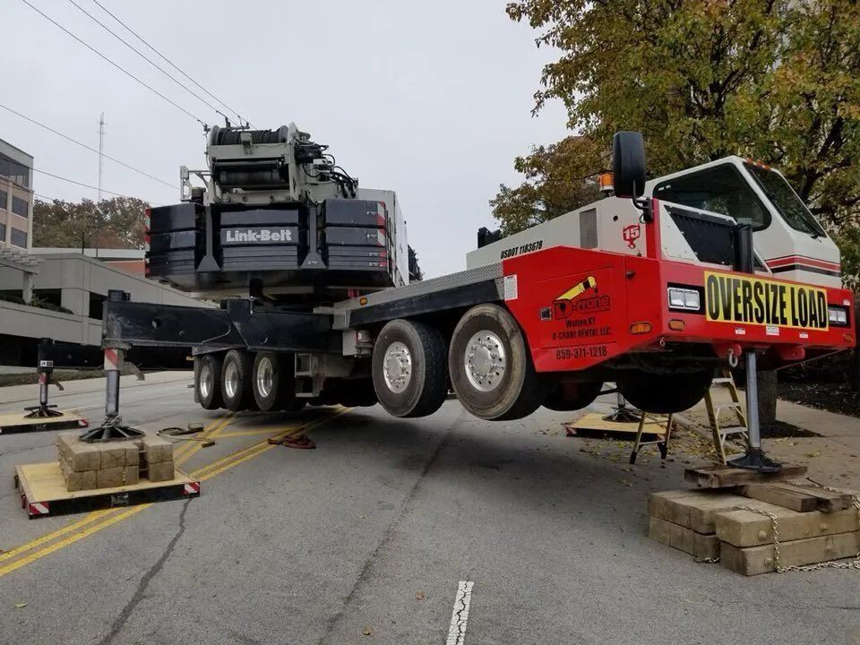 Oversized yellow heavy equipment trailer carrying machinery, parked on a city street with support jacks and blocks