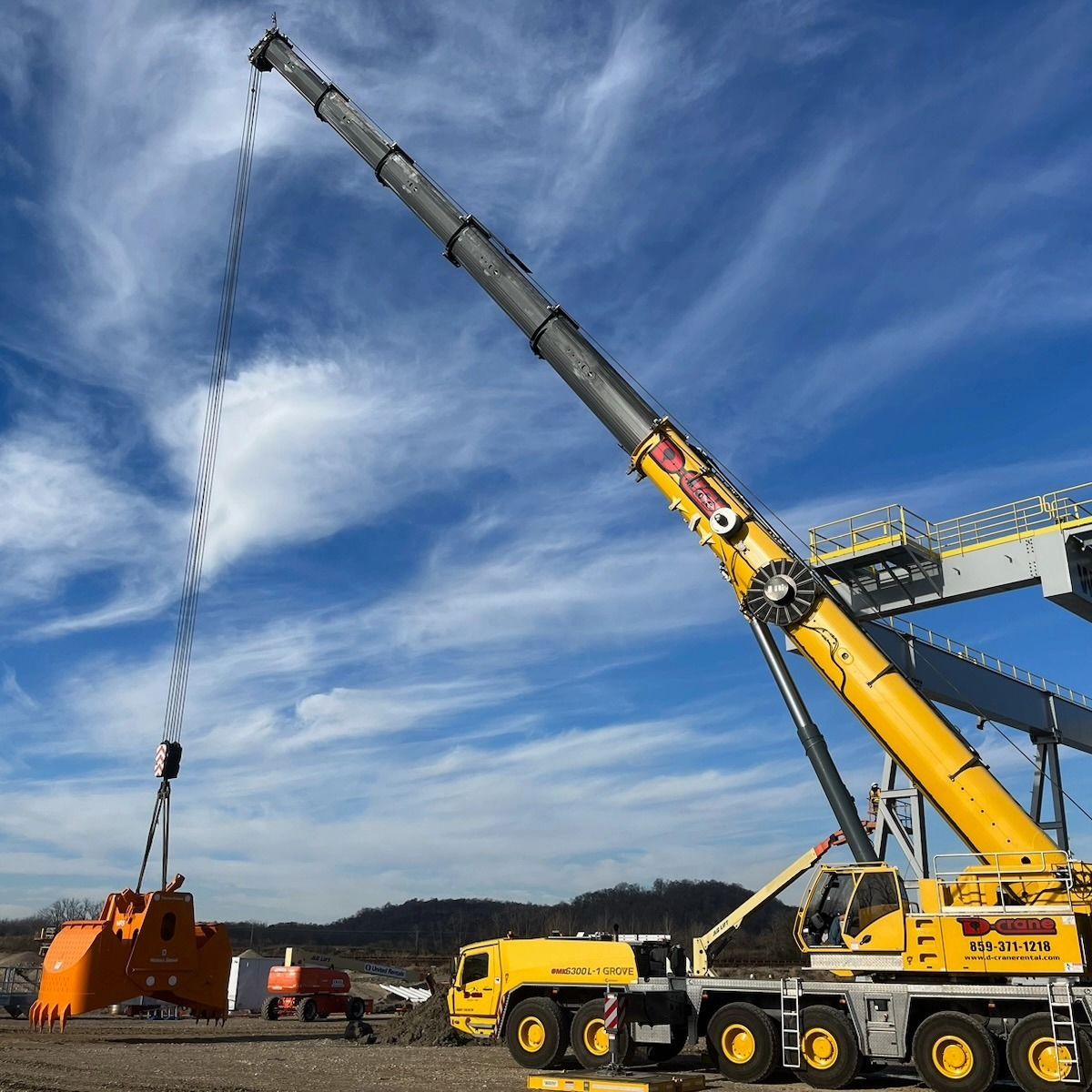 Yellow mobile crane lifting a load with a long extended boom under a blue sky