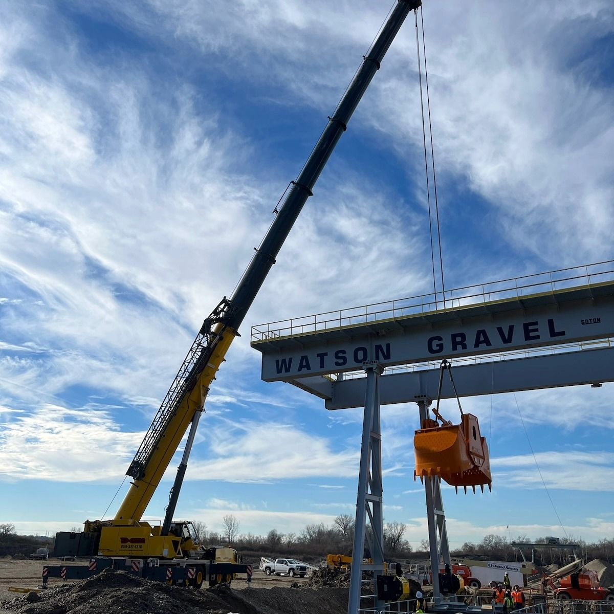 Crane lifting a Watson Gravel sign at a construction site under a cloudy sky