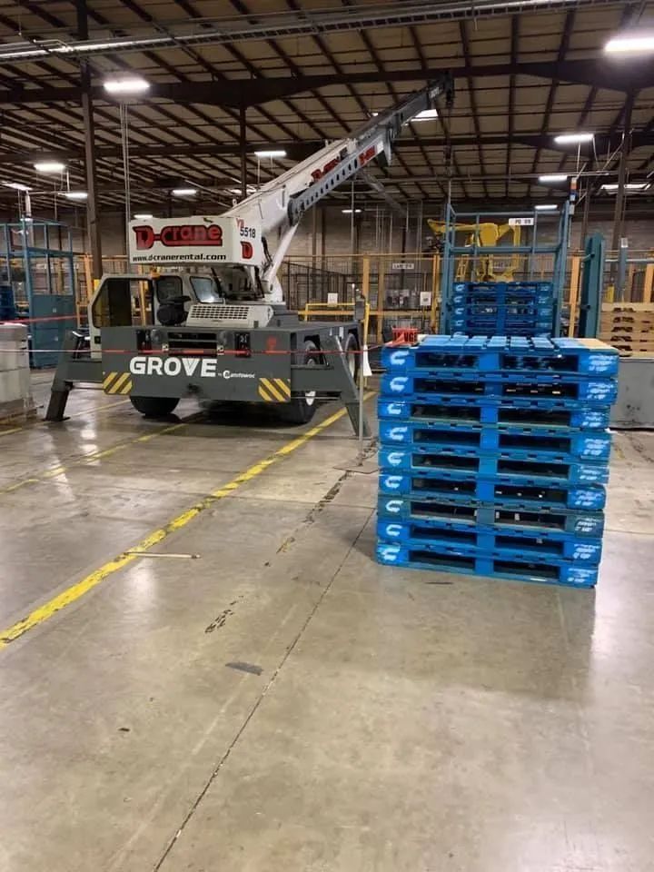 Warehouse with a Grove crane beside stacked blue pallets under an industrial ceiling