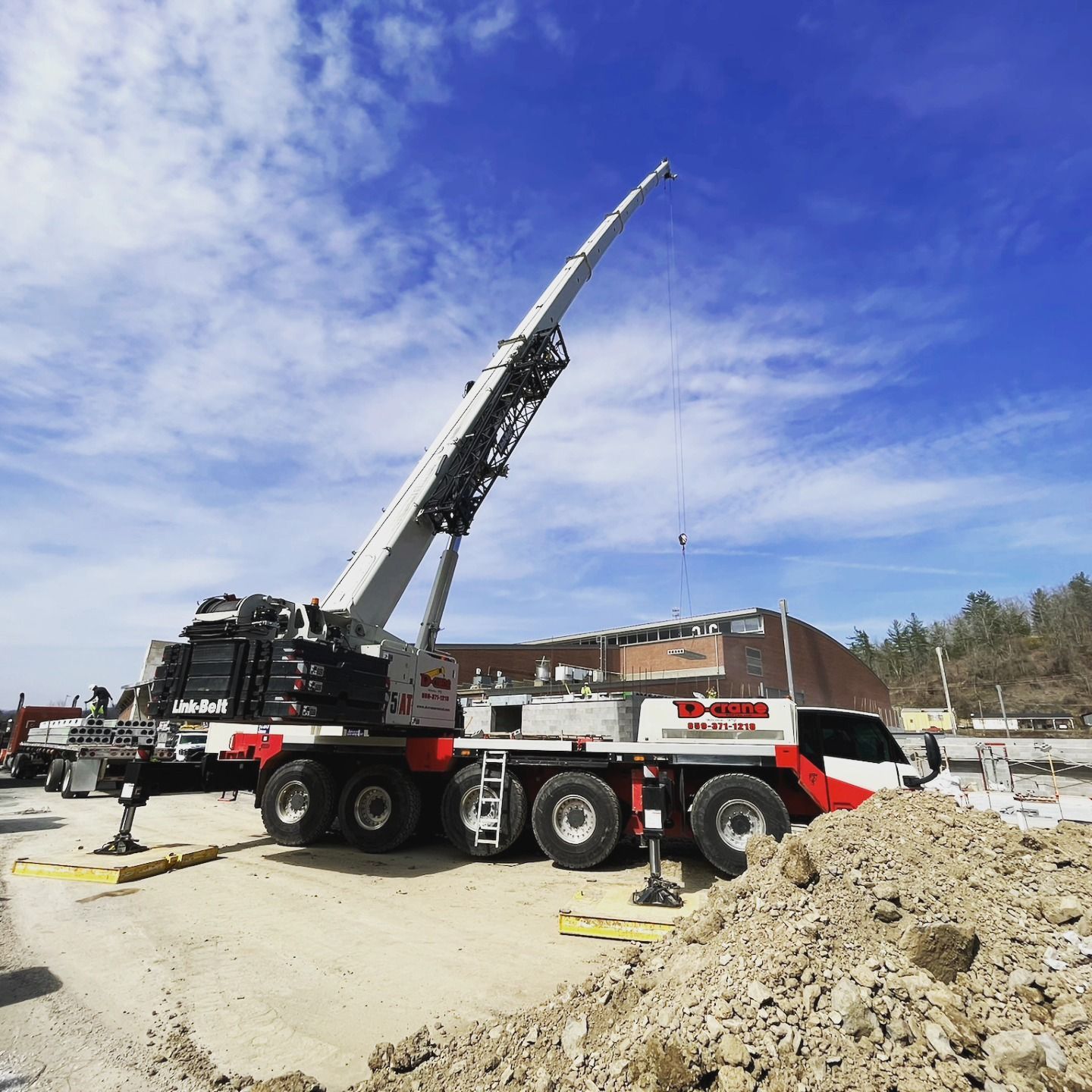 Large crane truck lifting its boom at a construction site under a blue sky