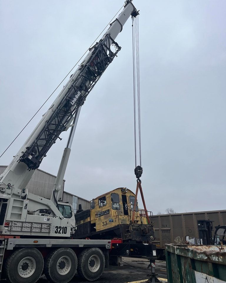 Crane lifting a yellow locomotive beside a railway yard under a cloudy sky