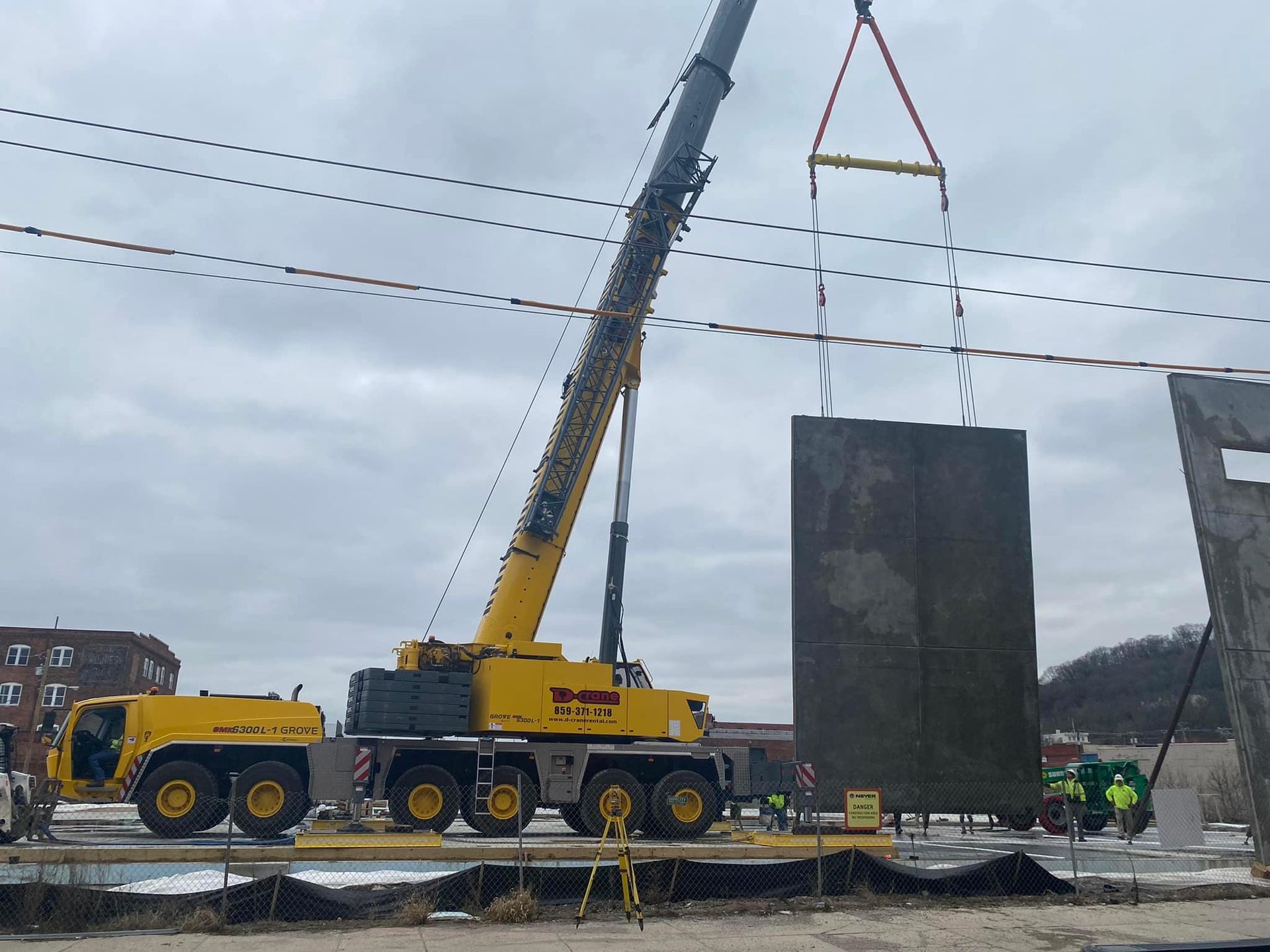 Yellow crane lifting a large concrete slab at a construction site under cloudy skies
