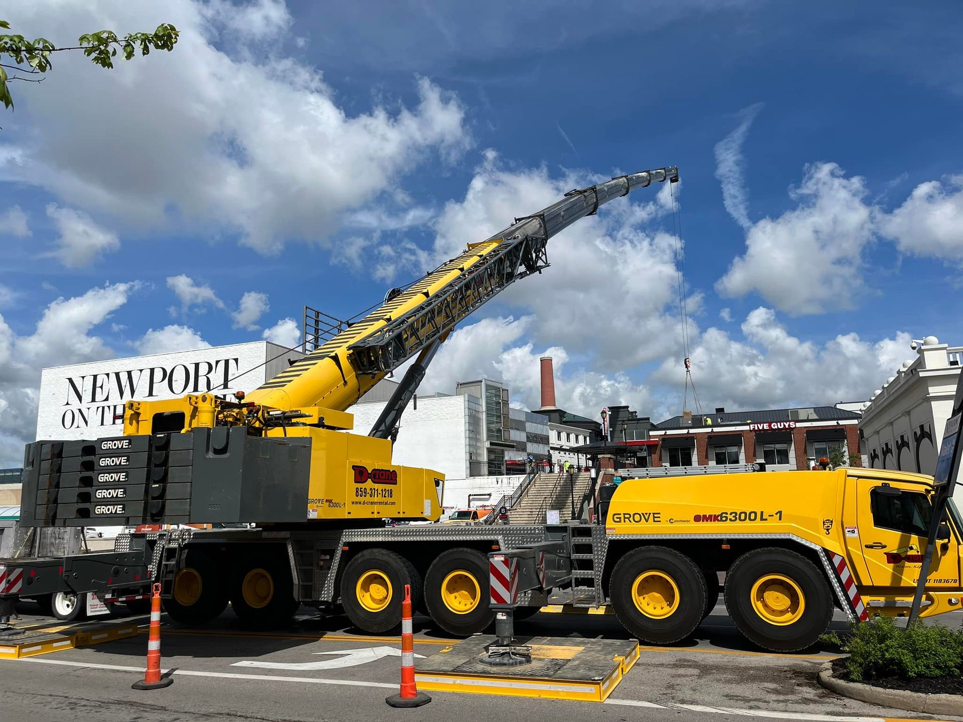 Yellow crane truck lifting equipment at a construction site under a blue sky