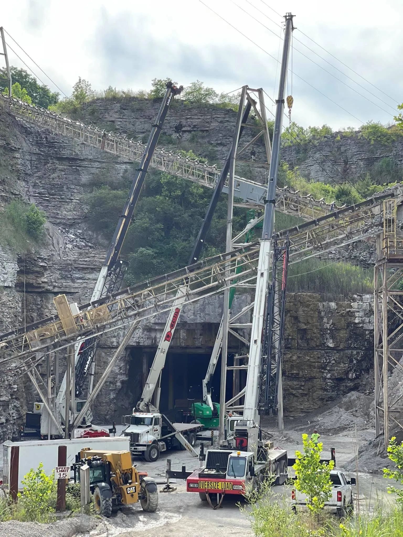 Construction workers and cranes at a tunnel entrance carved into a rocky hillside