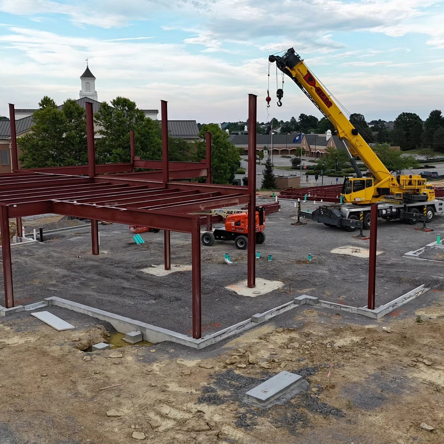 Construction site with a red steel frame and a yellow crane under a partly cloudy sky.