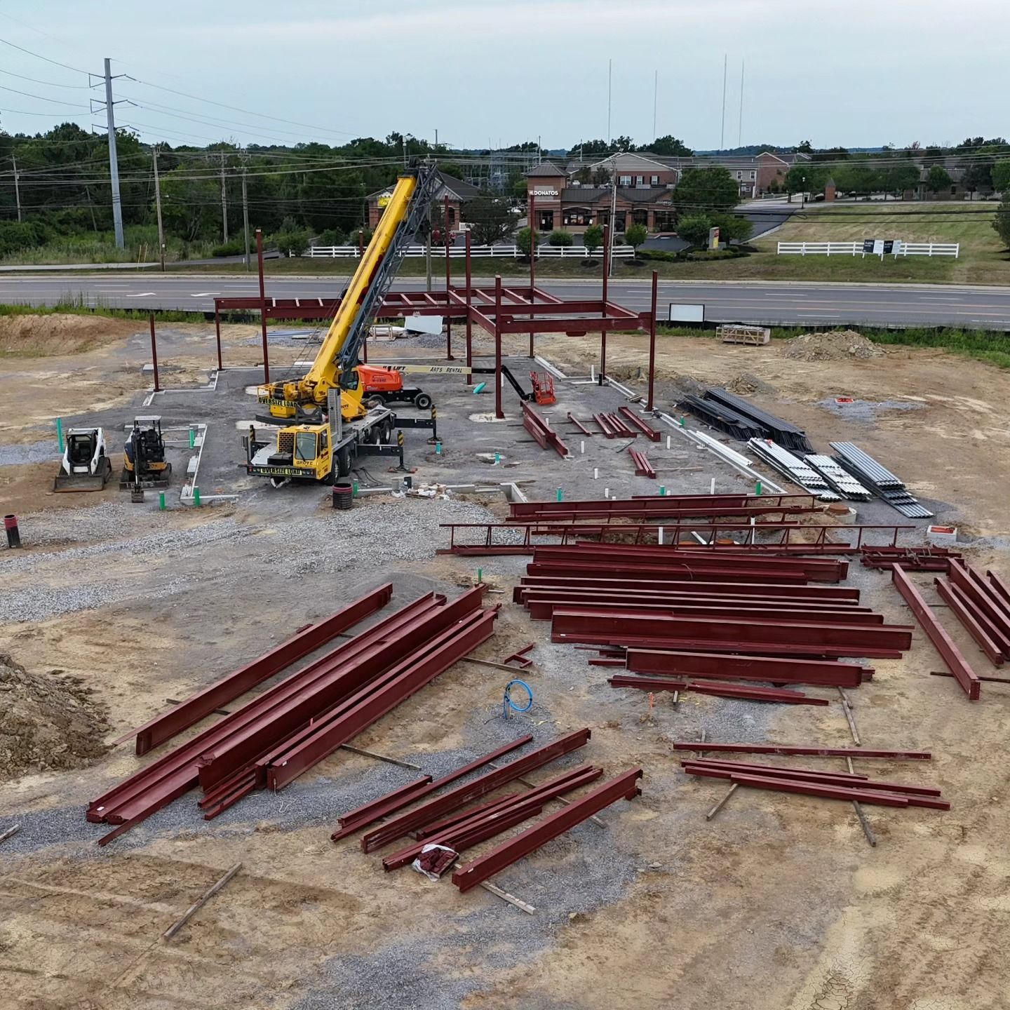 Construction site with yellow crane and red steel beams laid out on gravel.