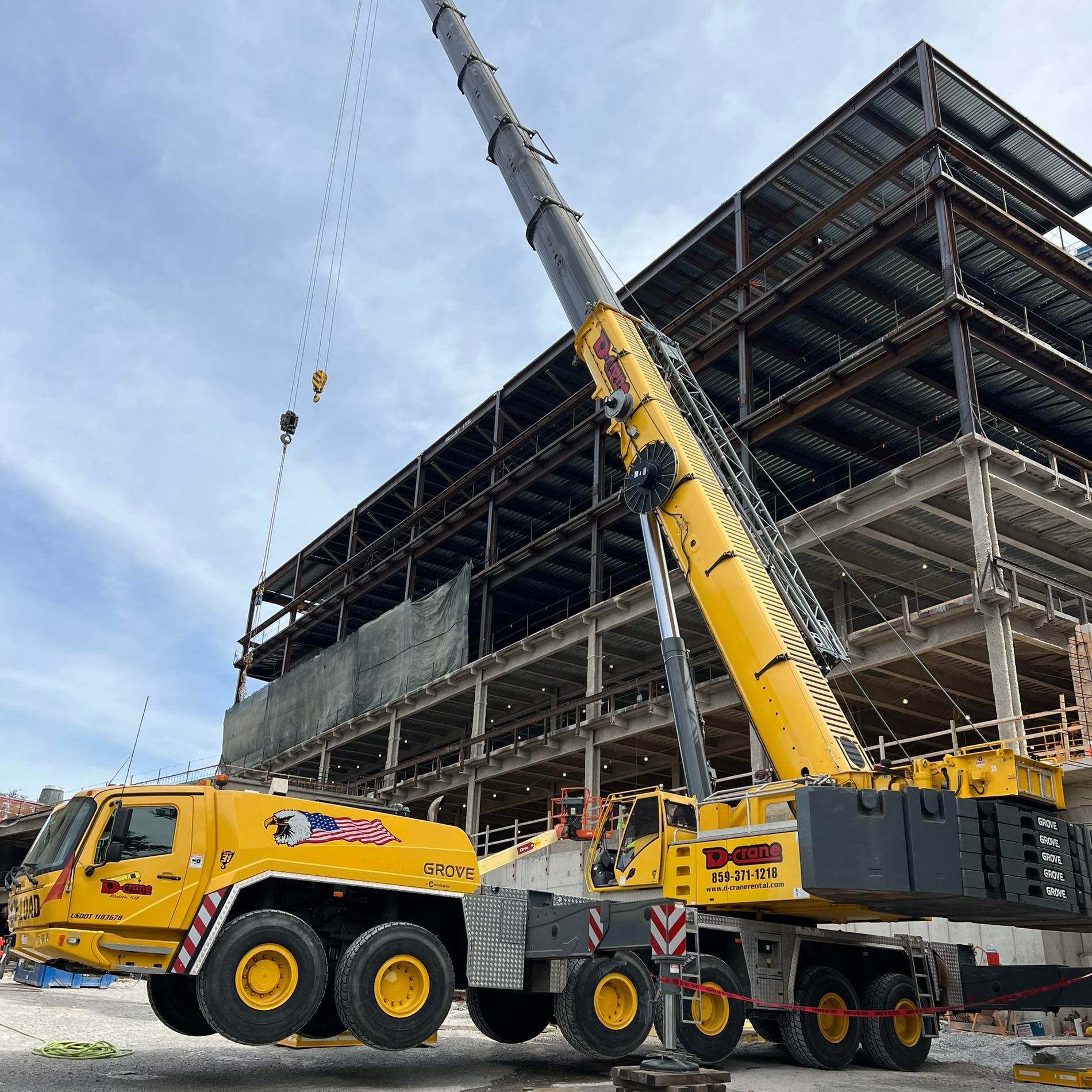 Yellow crane lifting steel at a multi-story construction site under a partly cloudy sky