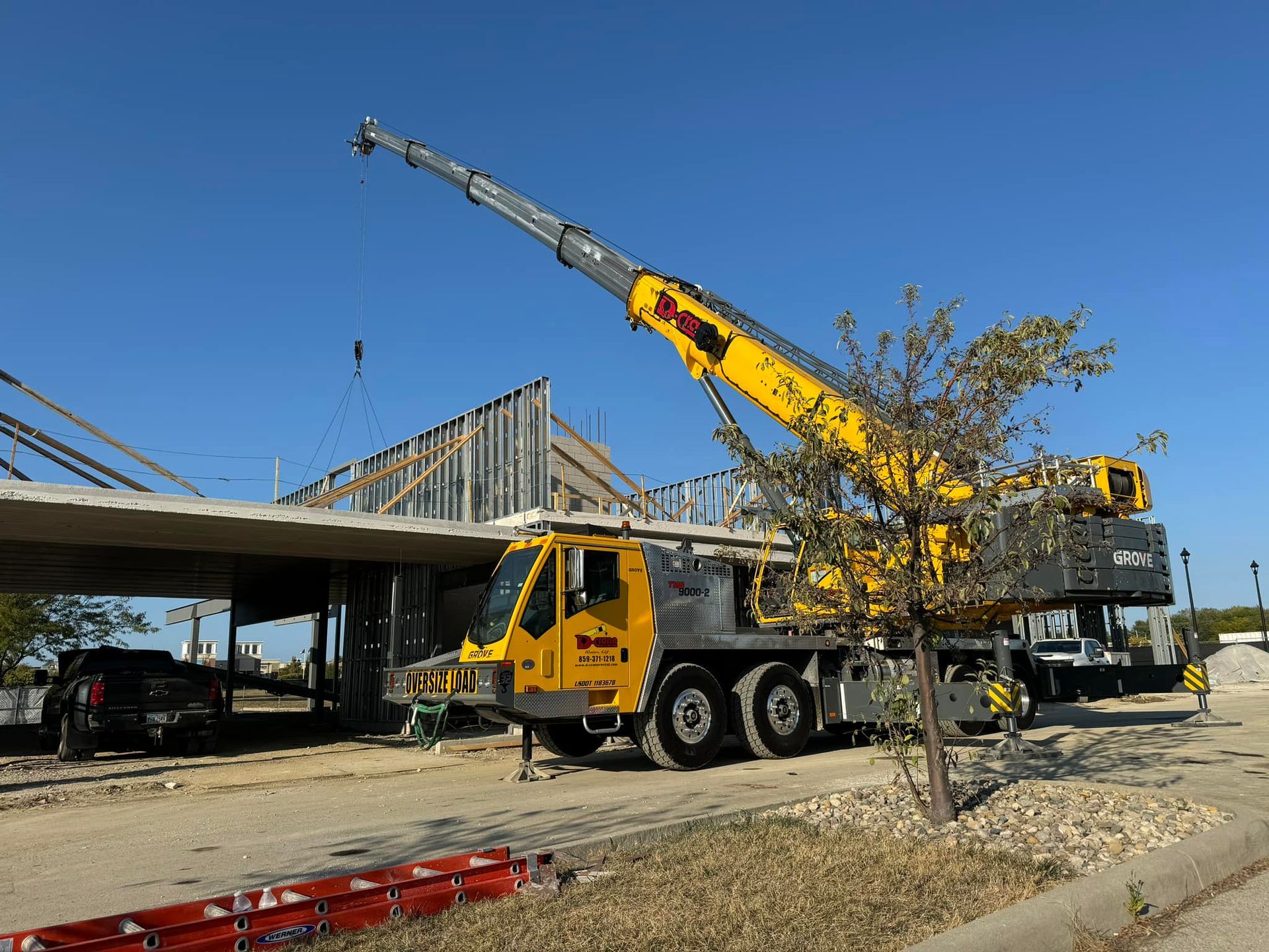Yellow crane truck lifting steel beams at a construction site under a clear blue sky