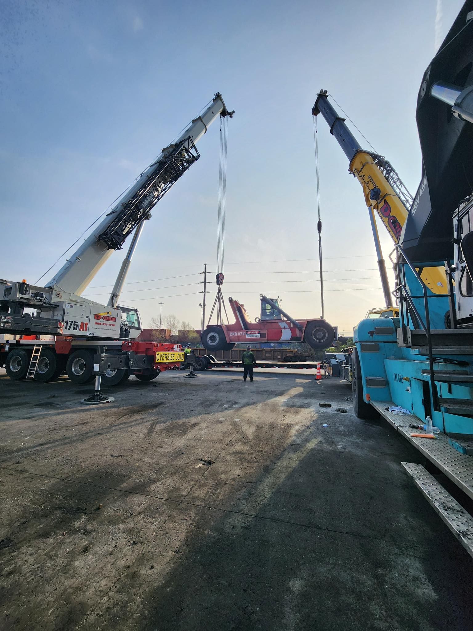 Crane trucks and lifting equipment at an outdoor construction site at dawn or dusk.