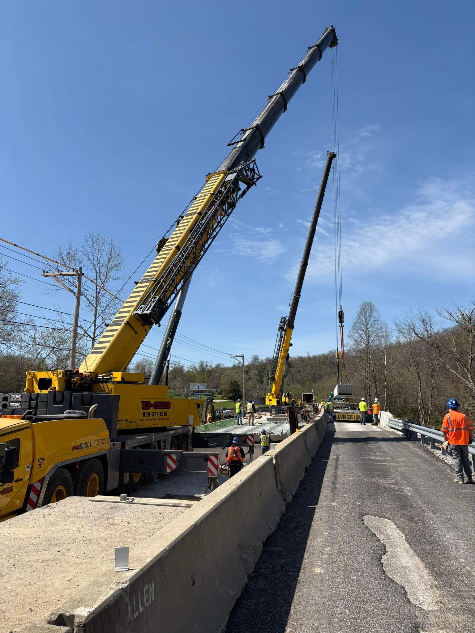 Two cranes lifting concrete barriers on a road construction site under a blue sky