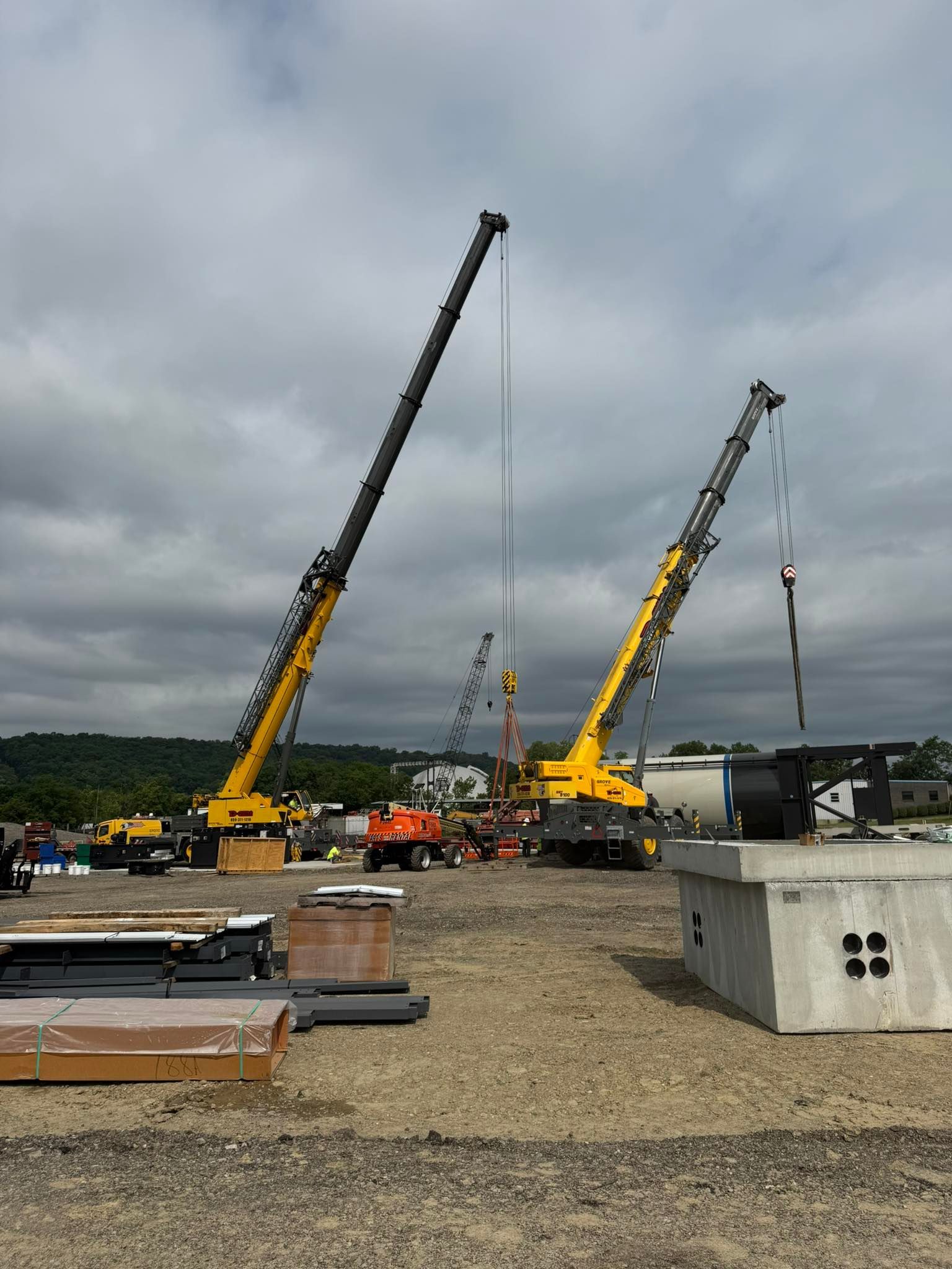 Two yellow cranes at a construction site under cloudy skies, with equipment and materials in the foreground