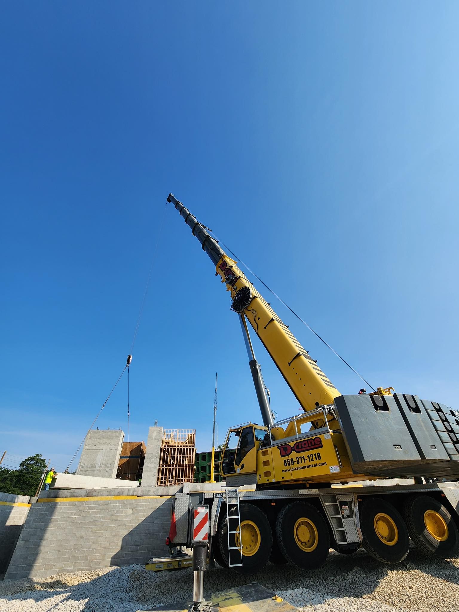 Yellow crane truck lifting a load on a construction site under a clear blue sky
