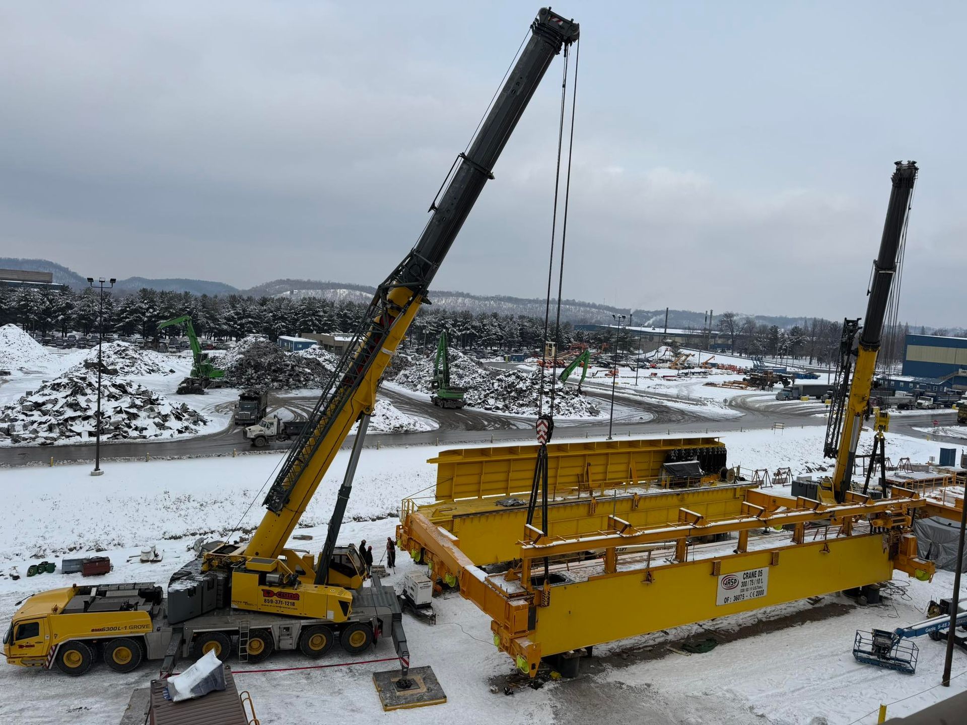 Two yellow cranes lifting a large yellow structure at a snowy construction site