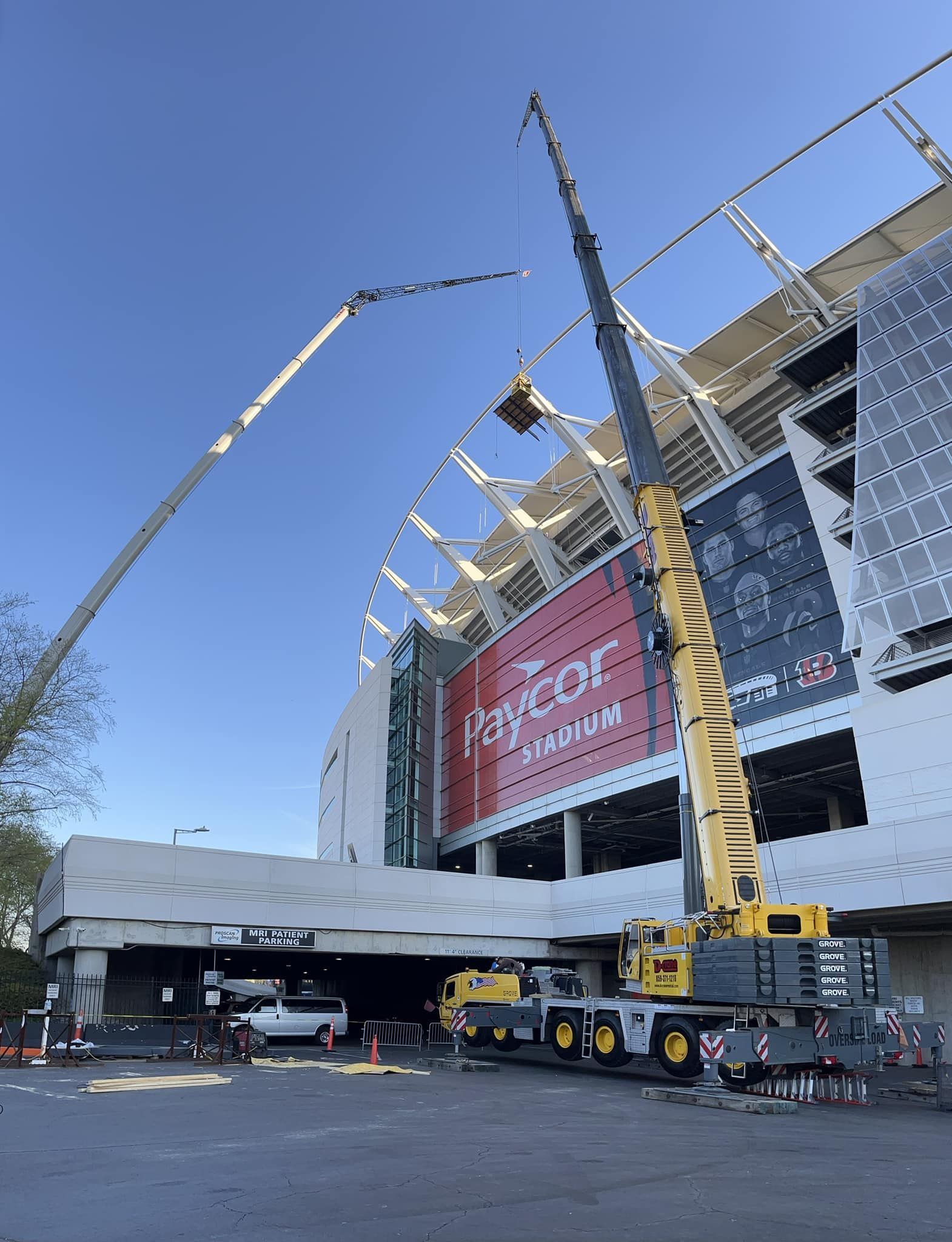Crane lifting steel at a stadium construction site under a blue sky