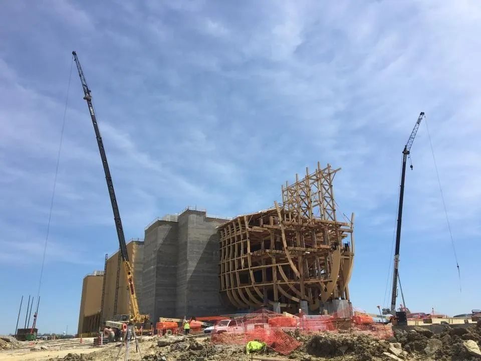 Construction site with tall crane booms and a large wooden framework on a building under a blue sky