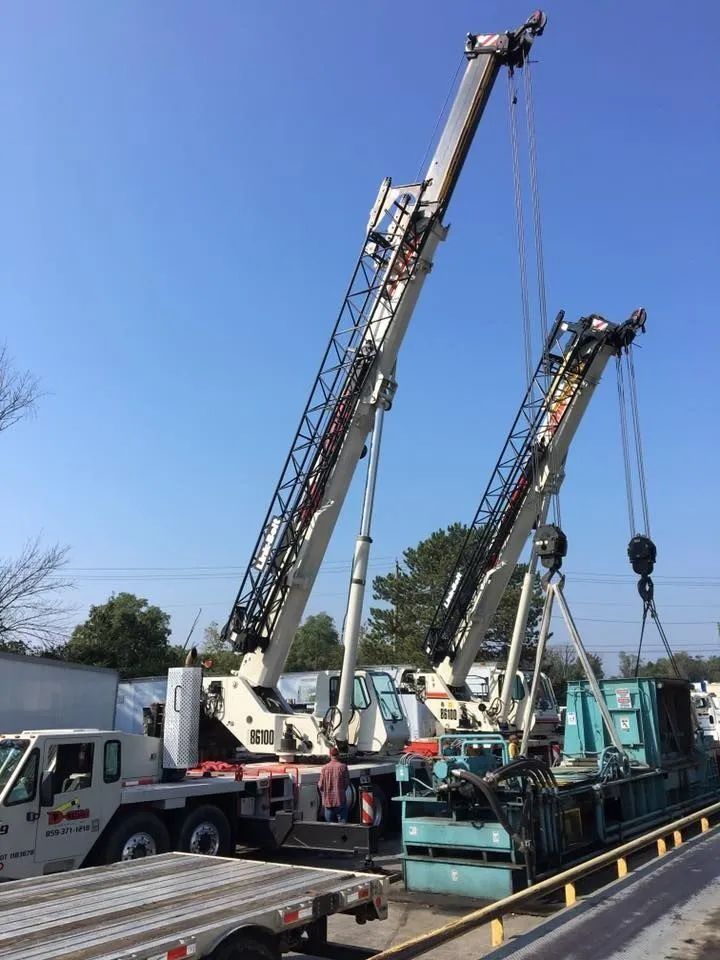 Two large mobile cranes lift equipment at a construction site under a clear blue sky.