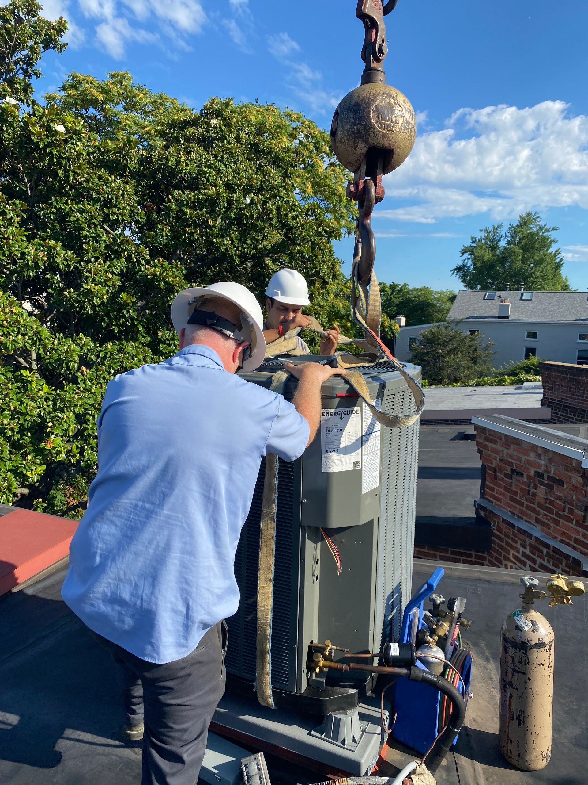 Two men are working on an air conditioner on a roof