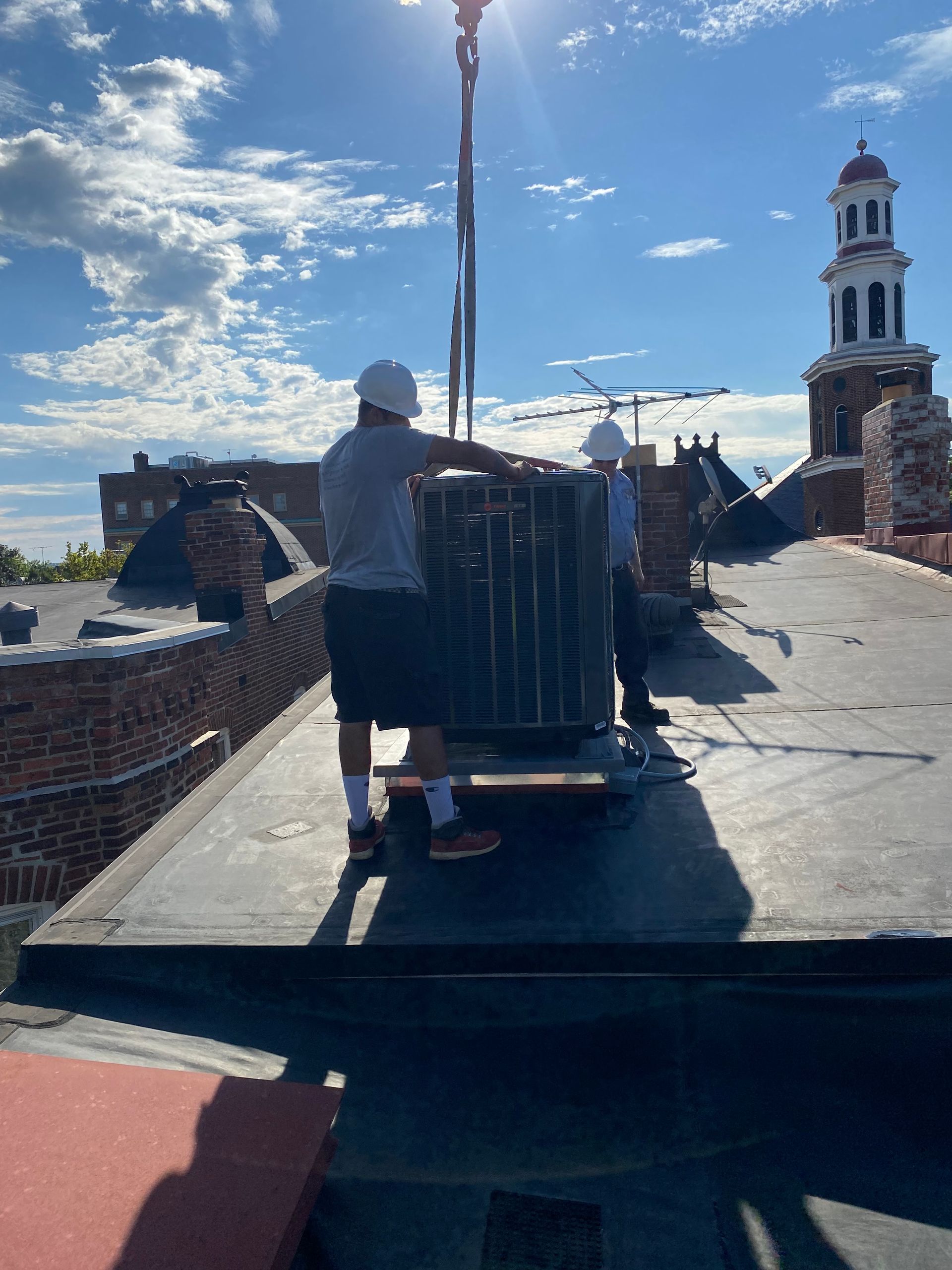 Two men are installing an AC unit on the roof of a building