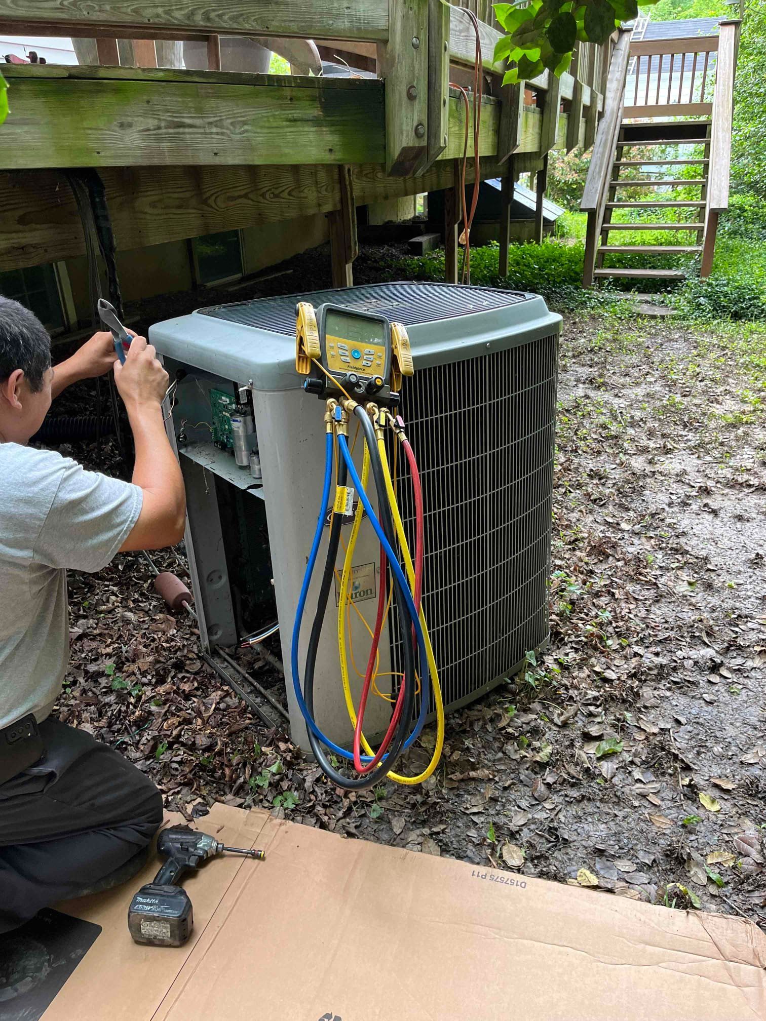 A man is working on an air conditioner outside of a house