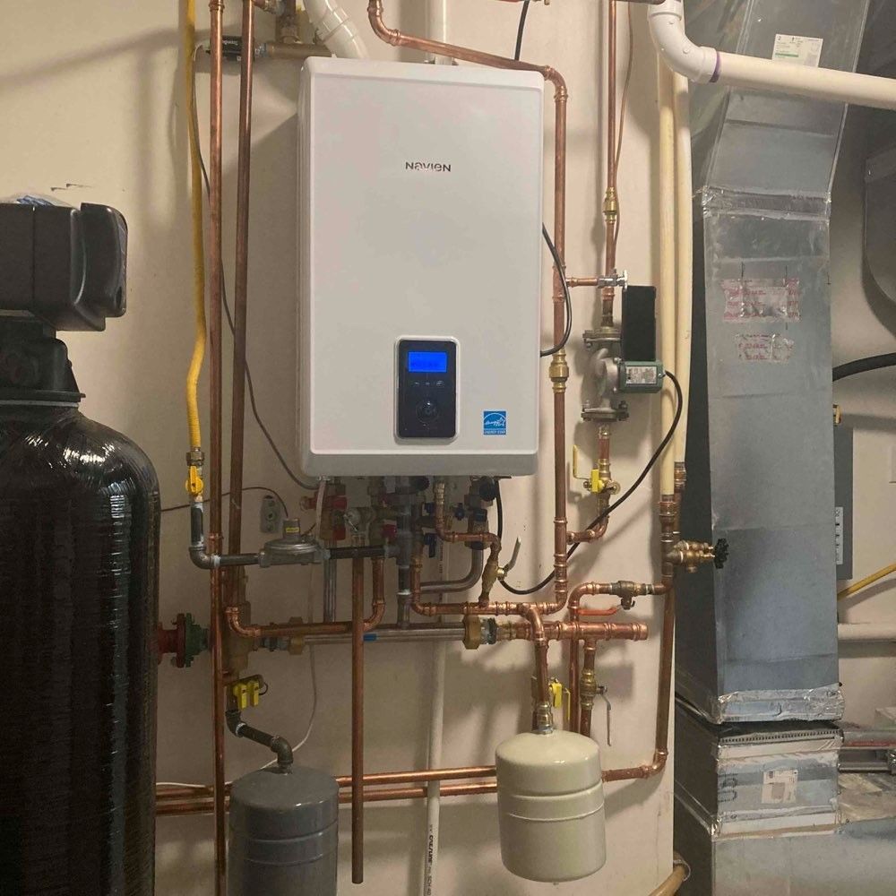 A white boiler is hanging on a wall connected to copper pipes