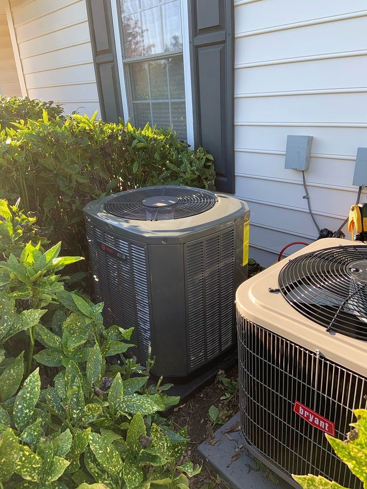 Two air conditioners are sitting next to each other on the side of a house