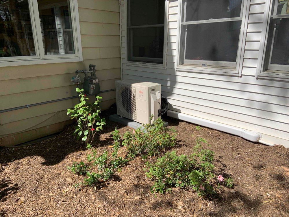 A house with a air conditioner in the backyard next to a window