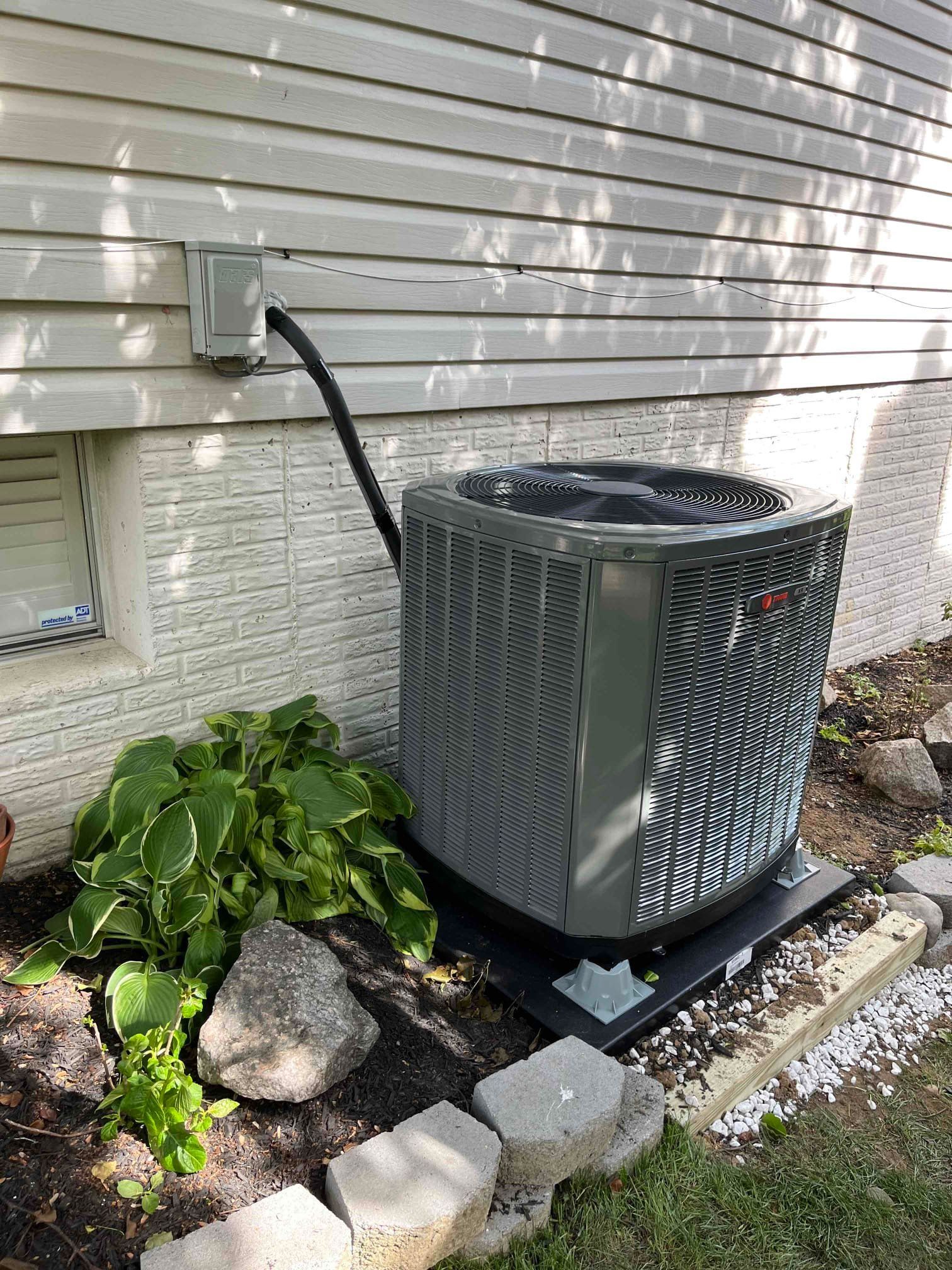 An air conditioner installed on the side of a house next to a window