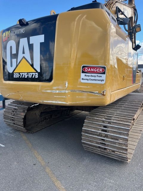 The back of a yellow Caterpillar excavator with a "Danger: Stay Clear of Moving Counterweight" warning sign.