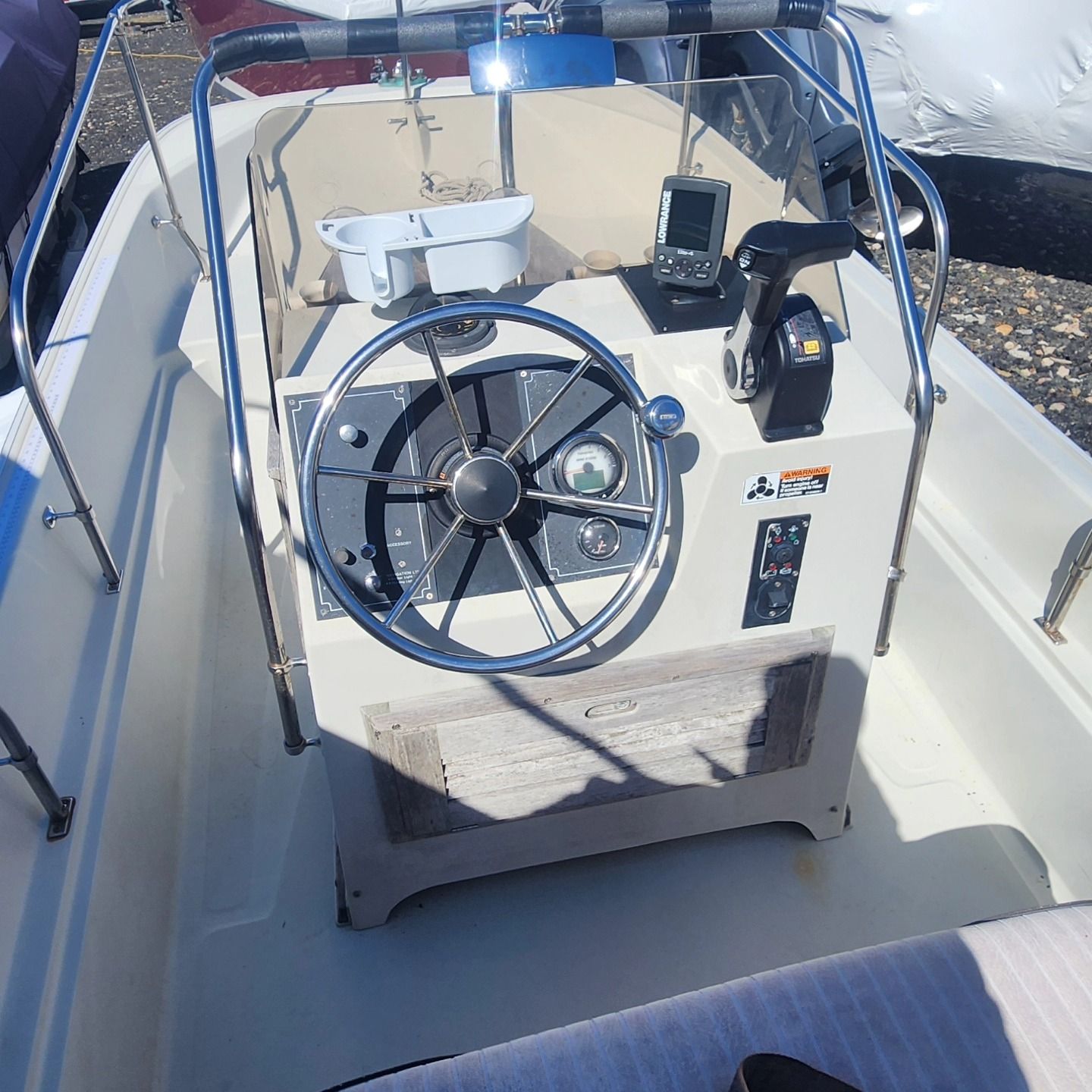 Boat's control panel: steering wheel, gauges, throttle, fish finder. Beige and white colors. Inside a boat.
