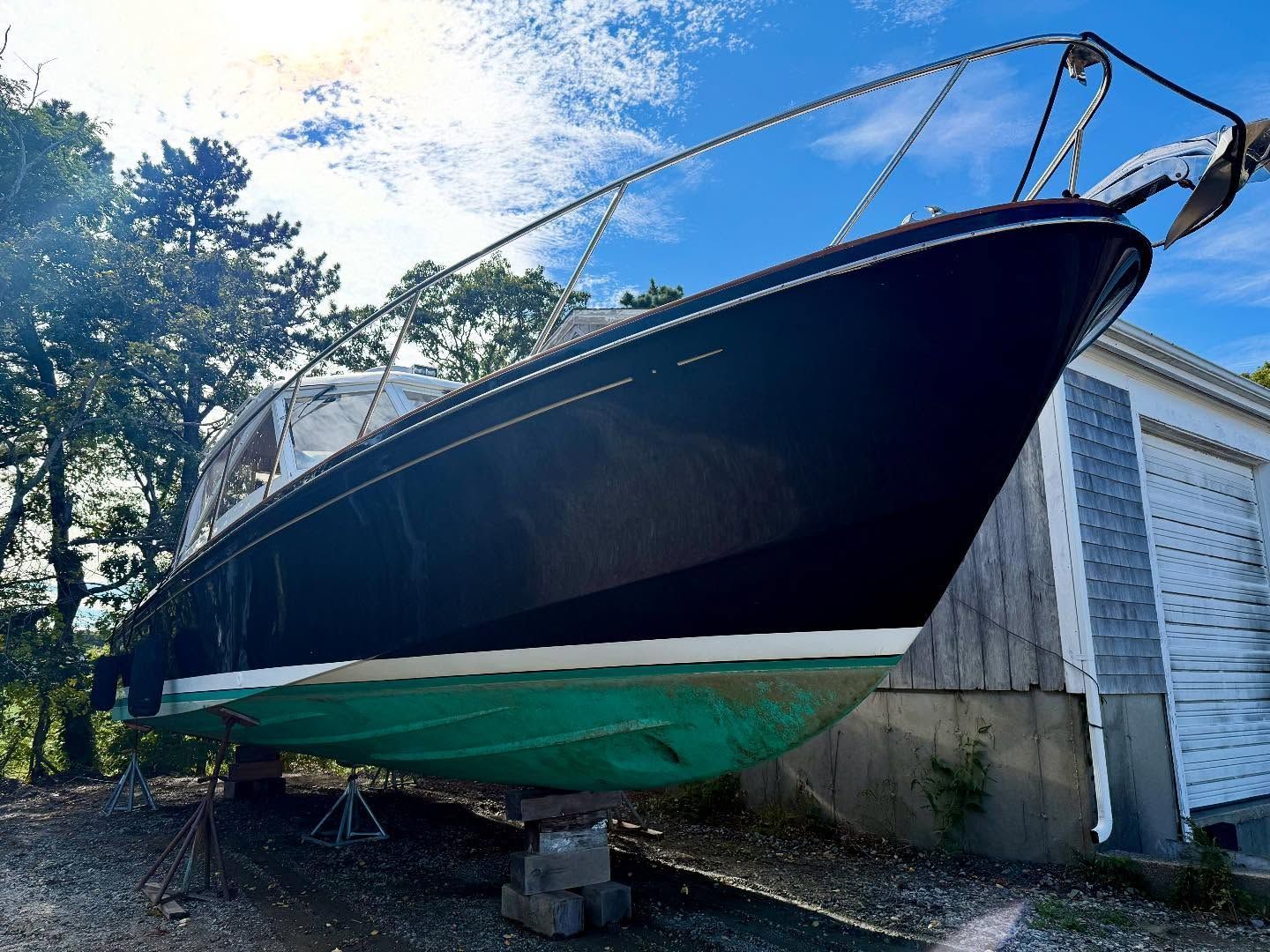 Black and white boat on blocks, green hull. Garage in the background, blue sky.
