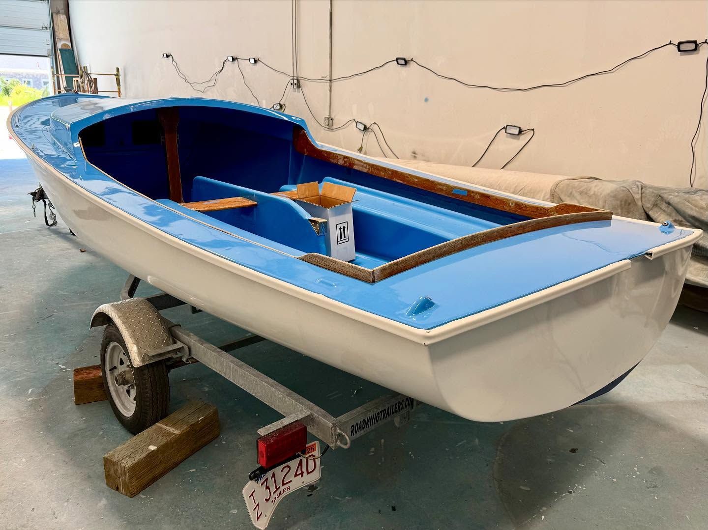A small blue and white boat on a trailer, inside a building.
