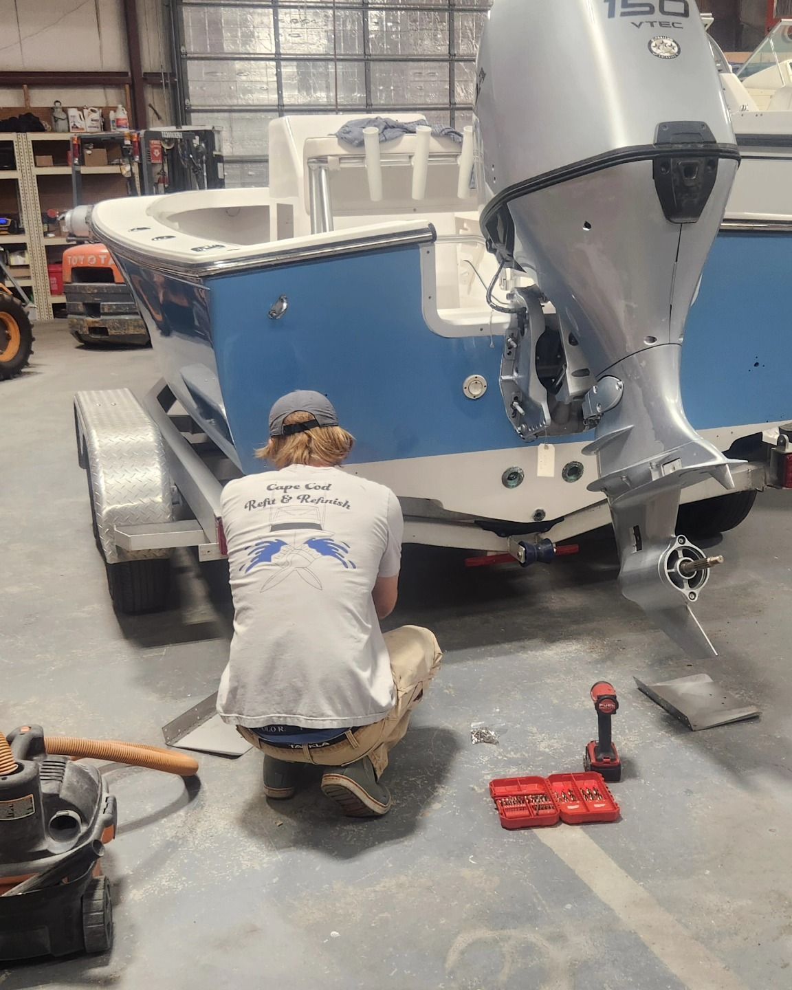 A person working on the engine of a boat on a trailer, inside a workshop.