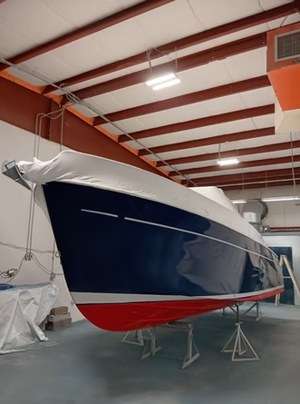 Blue and red boat covered in white tarp inside a building with a metal frame roof.