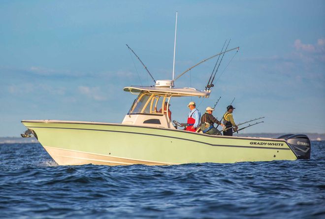 A light green fishing boat with four people on board, fishing on the water.