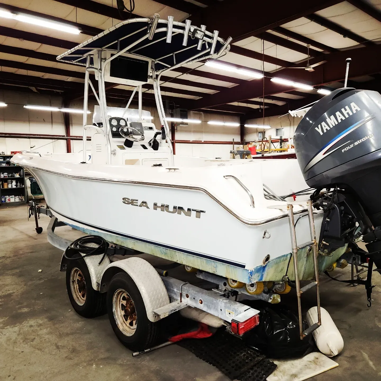 White Sea Hunt boat on a trailer, with a blue awning and a Yamaha motor in a garage setting.