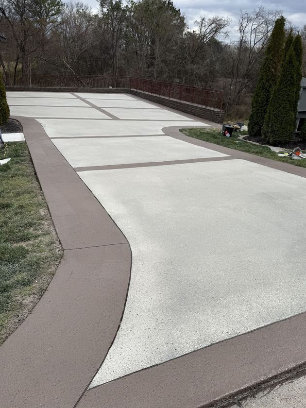 Freshly paved driveway with light concrete sections and brown borders beside grass and shrubs