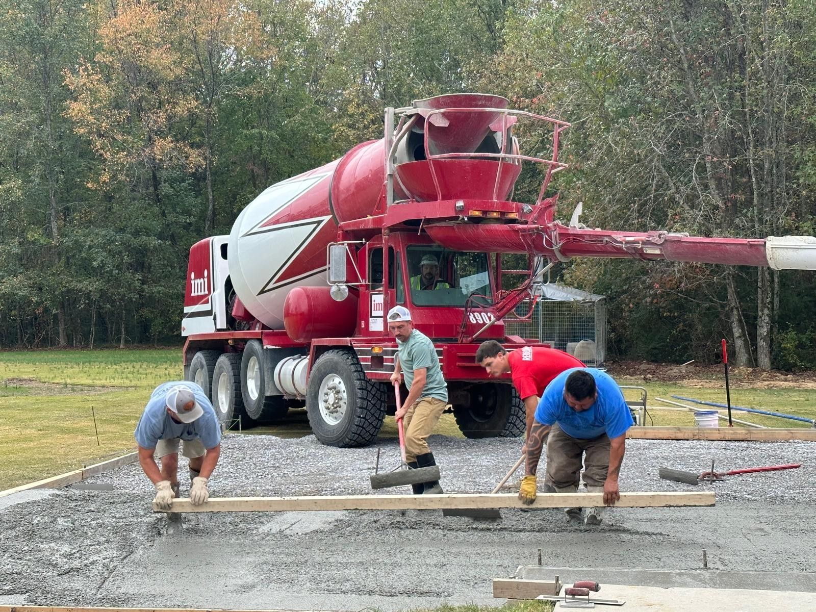 Workers pouring concrete beside a red cement mixer truck at an outdoor construction site