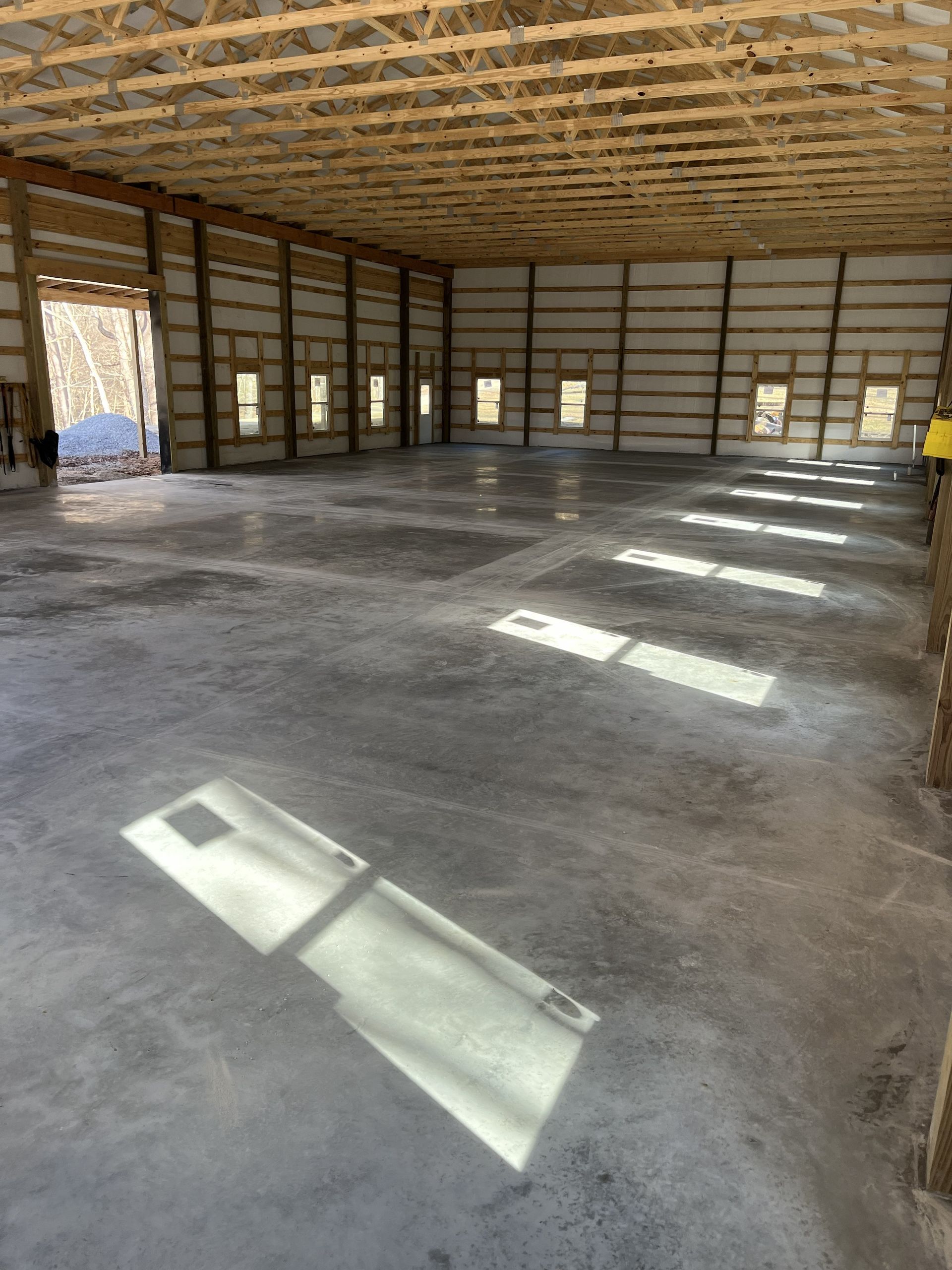 Empty unfinished room with exposed wood framing, concrete floor, and sunlight streaming through windows.