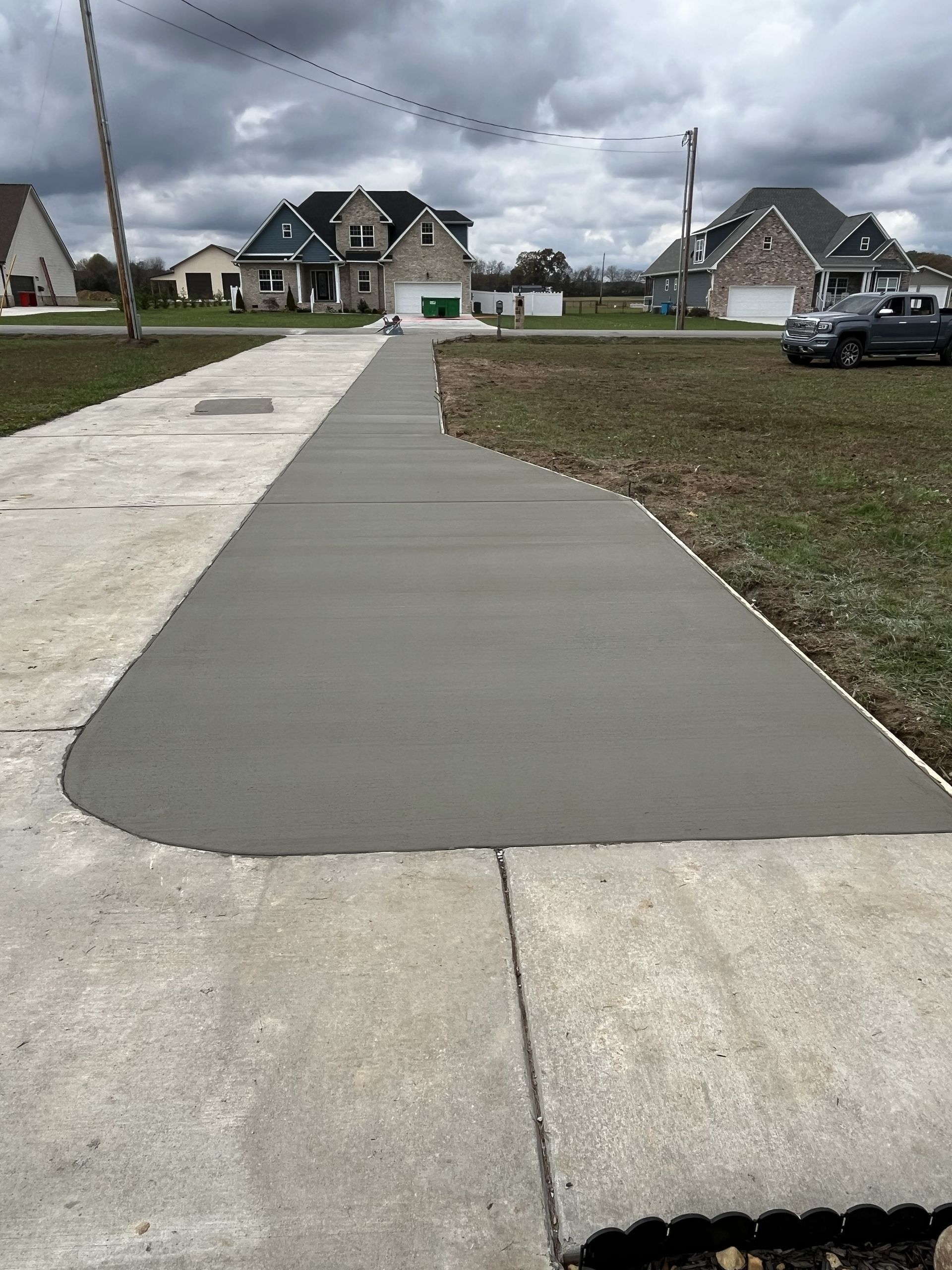 Freshly poured concrete driveway section in a suburban neighborhood under cloudy skies