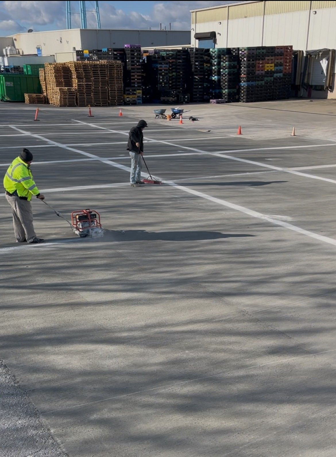 Workers marking lines in an empty parking lot with cones and carts.