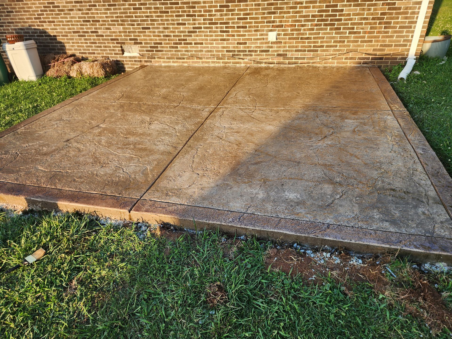 Concrete patio beside a brick wall, with grass and a white downspout on the right.