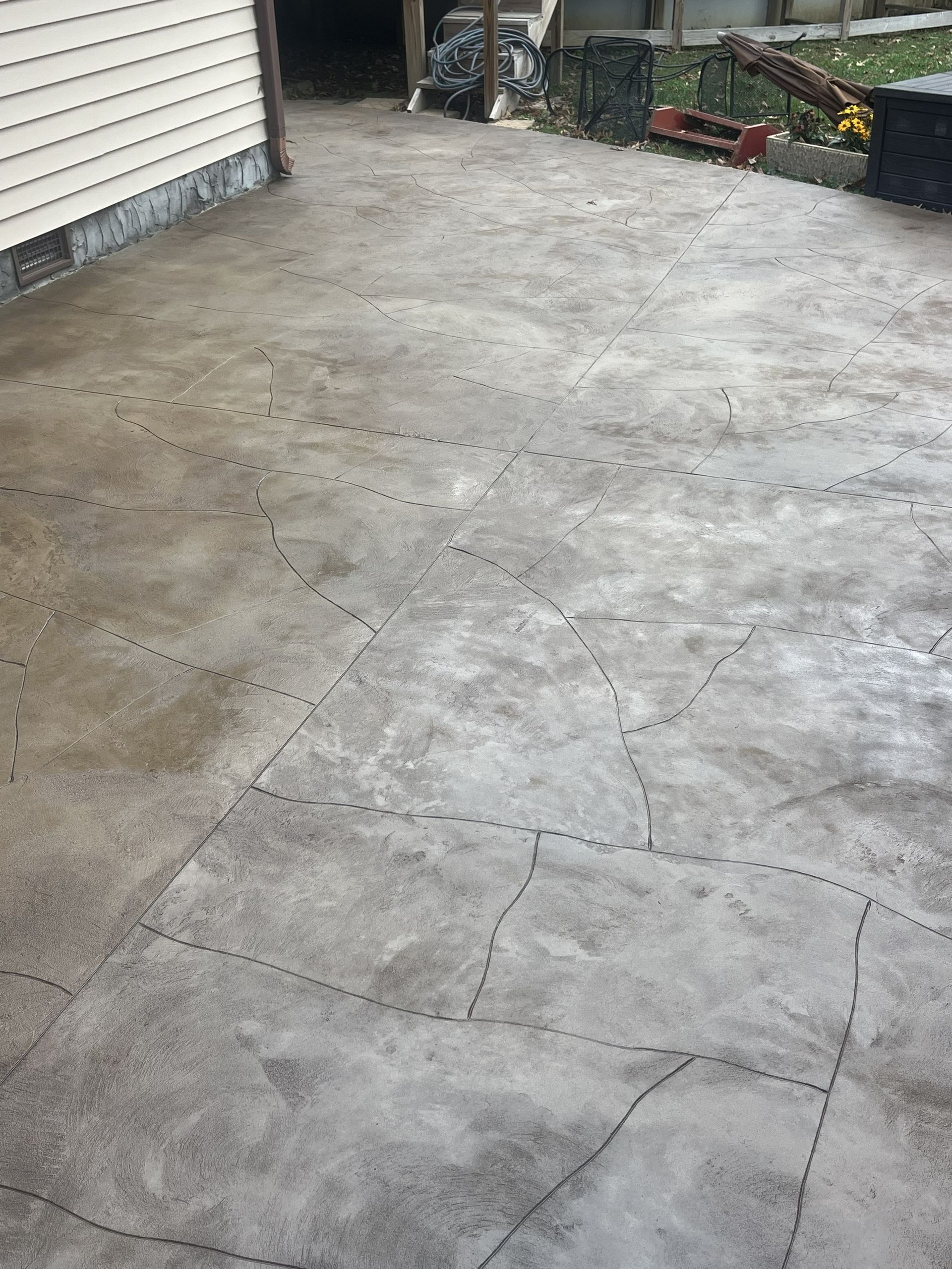 Concrete driveway next to a garage wall and garden edge with potted plants and tools