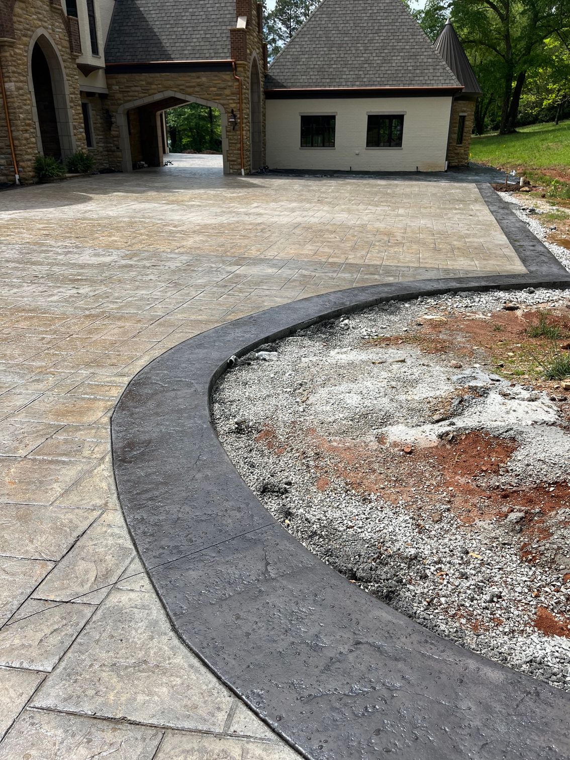 Curved dark stone border outlining a gravel bed beside a paved driveway and stone house exterior
