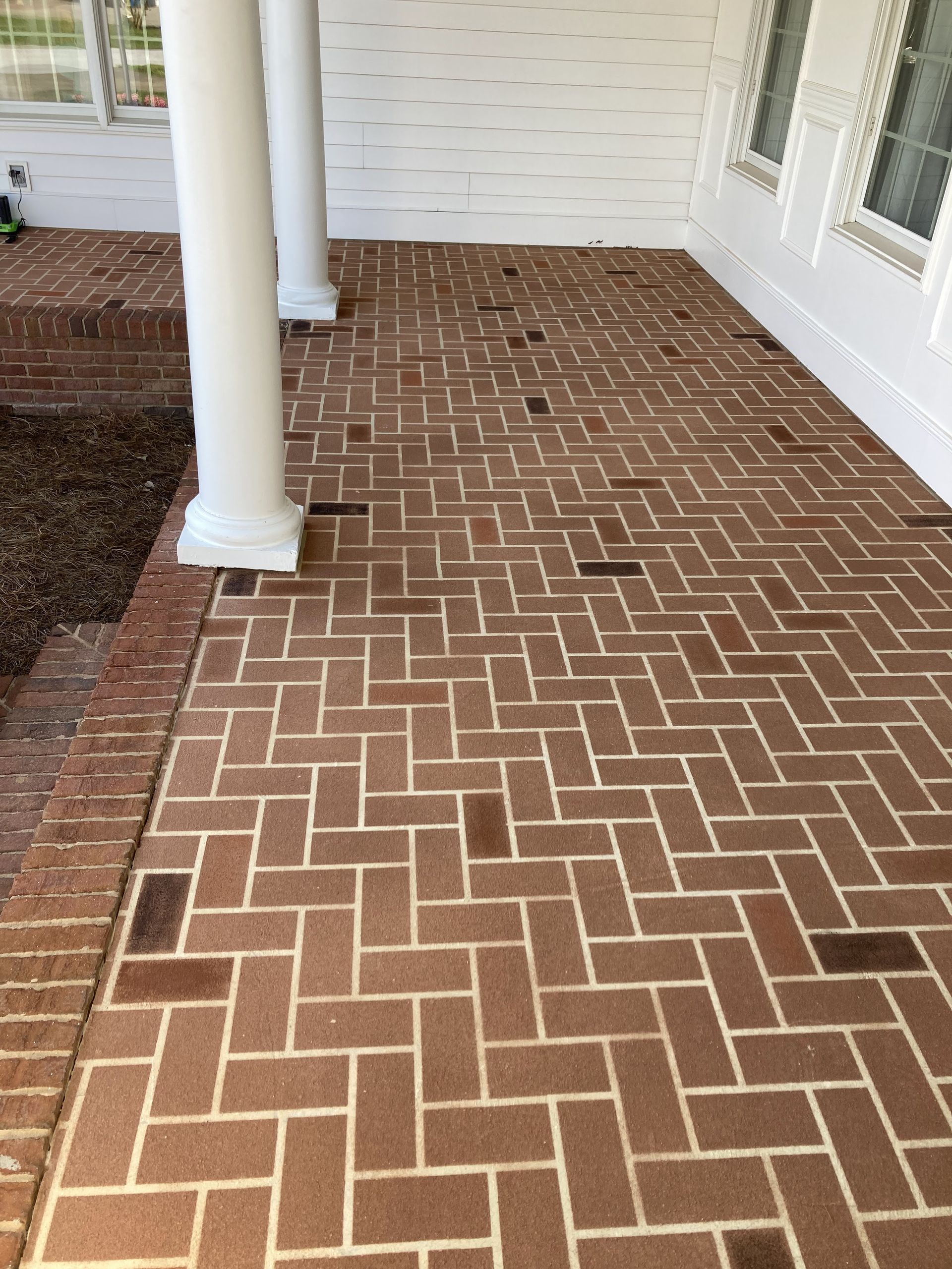 Brick herringbone porch floor with white columns and siding beside windows