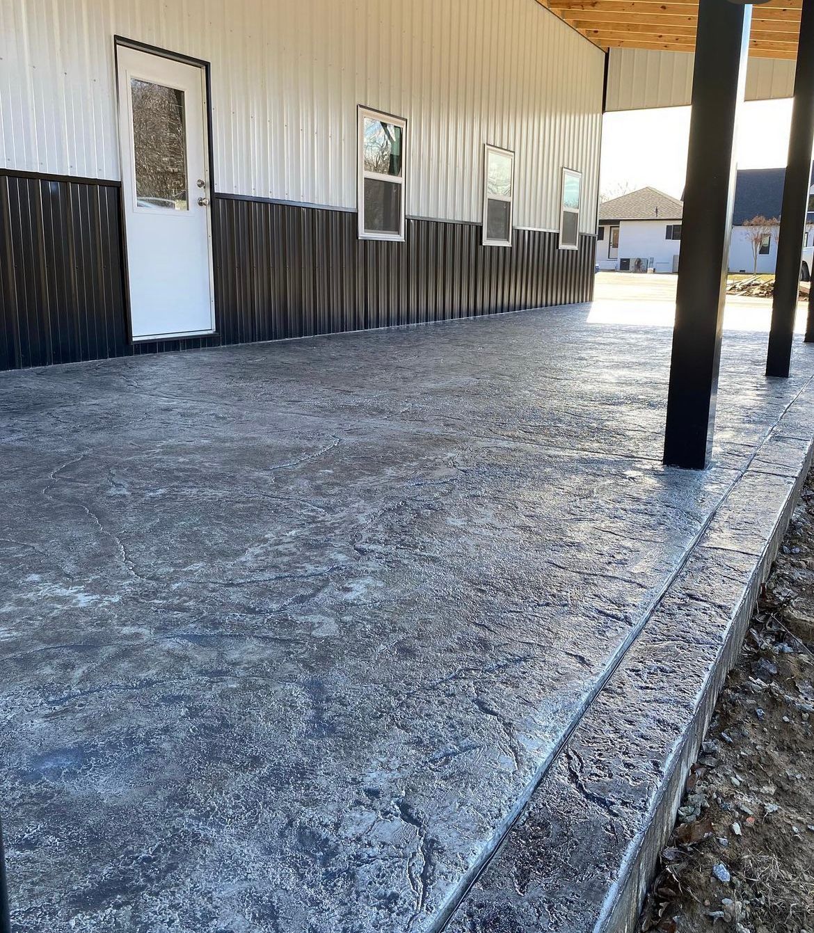 Gravel-covered patio beside a corrugated metal building with windows and black support posts