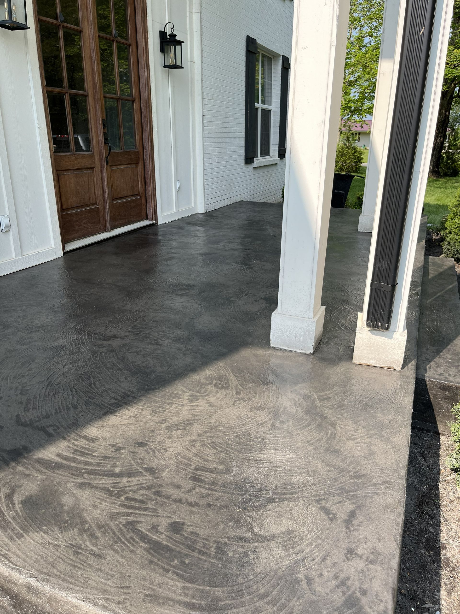 Front porch with white columns, dark wooden door, and sunlit concrete floor.