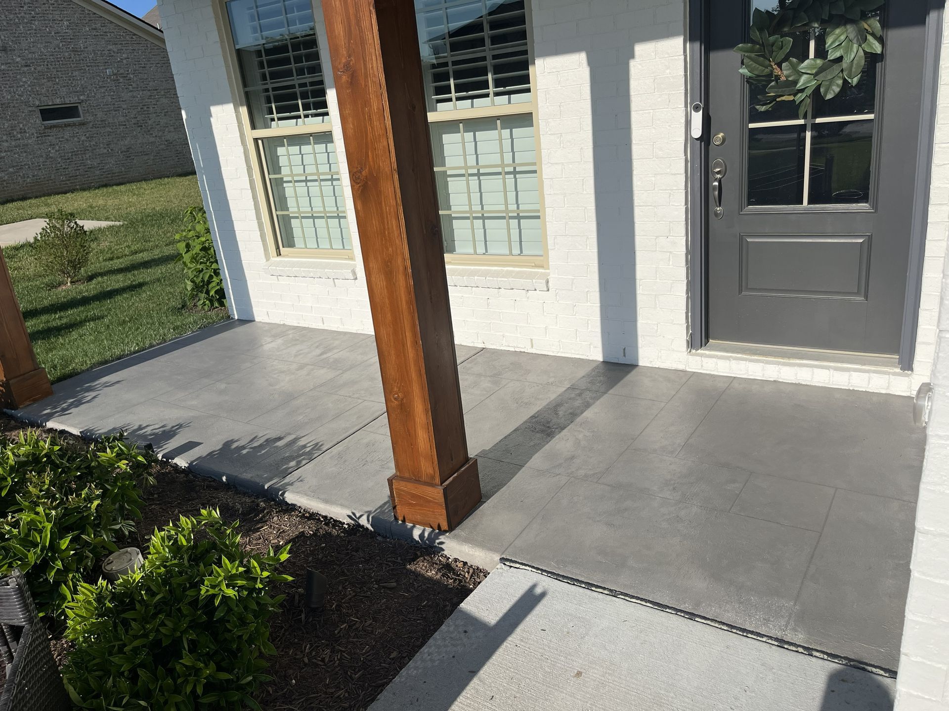 Front porch with gray concrete, wooden post, white siding, and a dark front door beside windows.