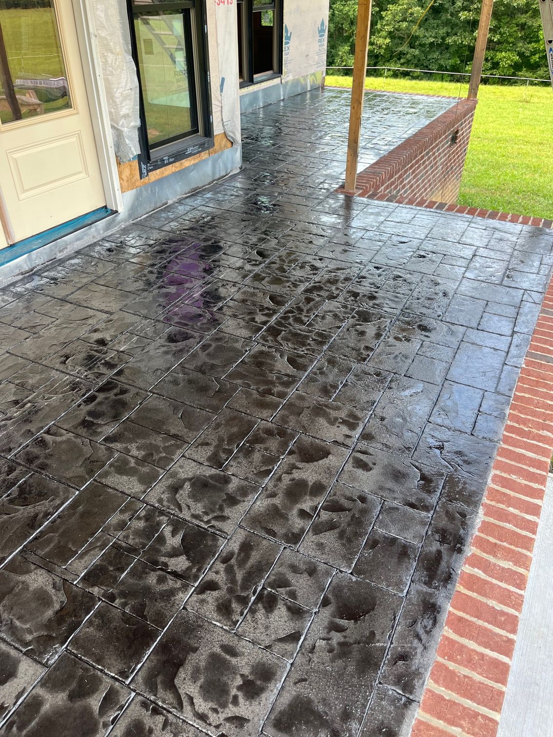 Rain-slick brick patio beside a house, with an open doorway and green lawn beyond.