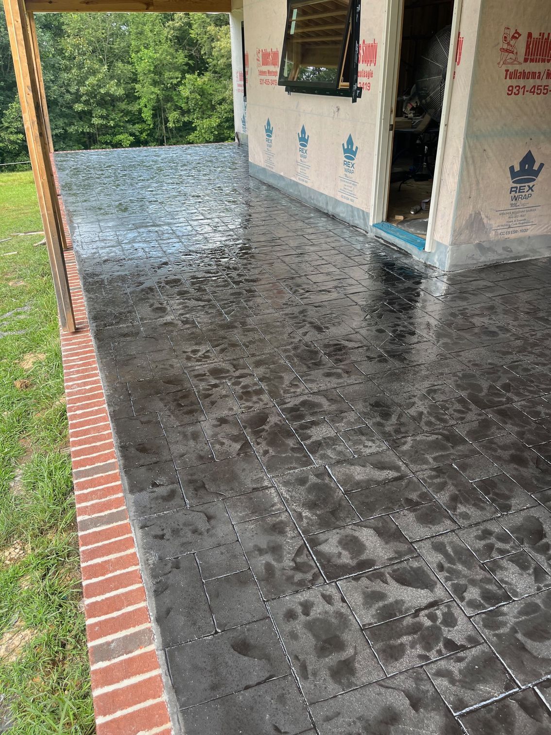 Covered porch with dark tiled floor, brick edging, and a view of greenery outside.